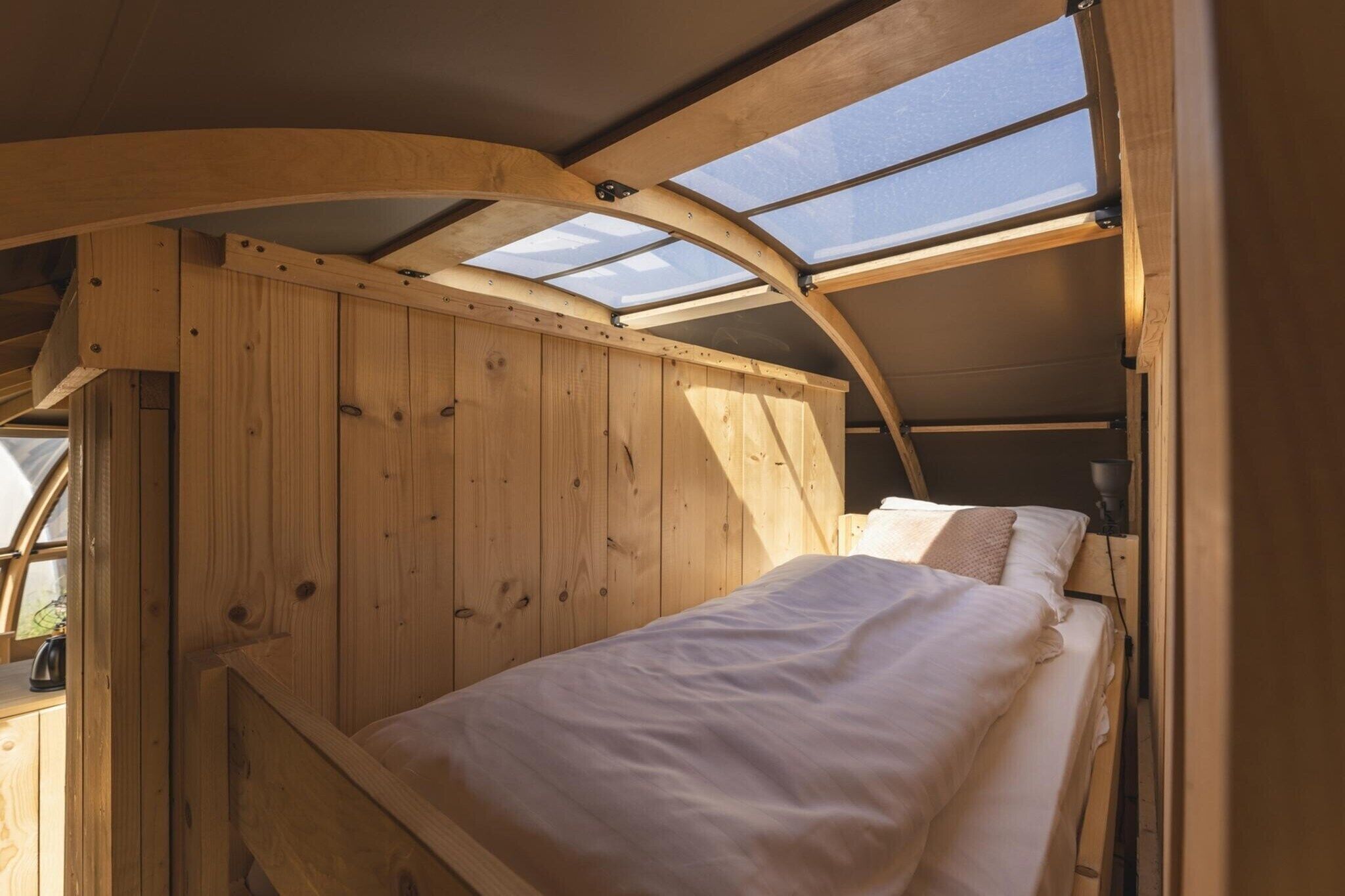 A wooden interior with a curved ceiling, a bed, and skylights.