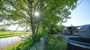 A camping area with a wooden deck, a hot tub, and a view of a water body. - Unique Riverdome Stay with Hot Tub (Zuna)