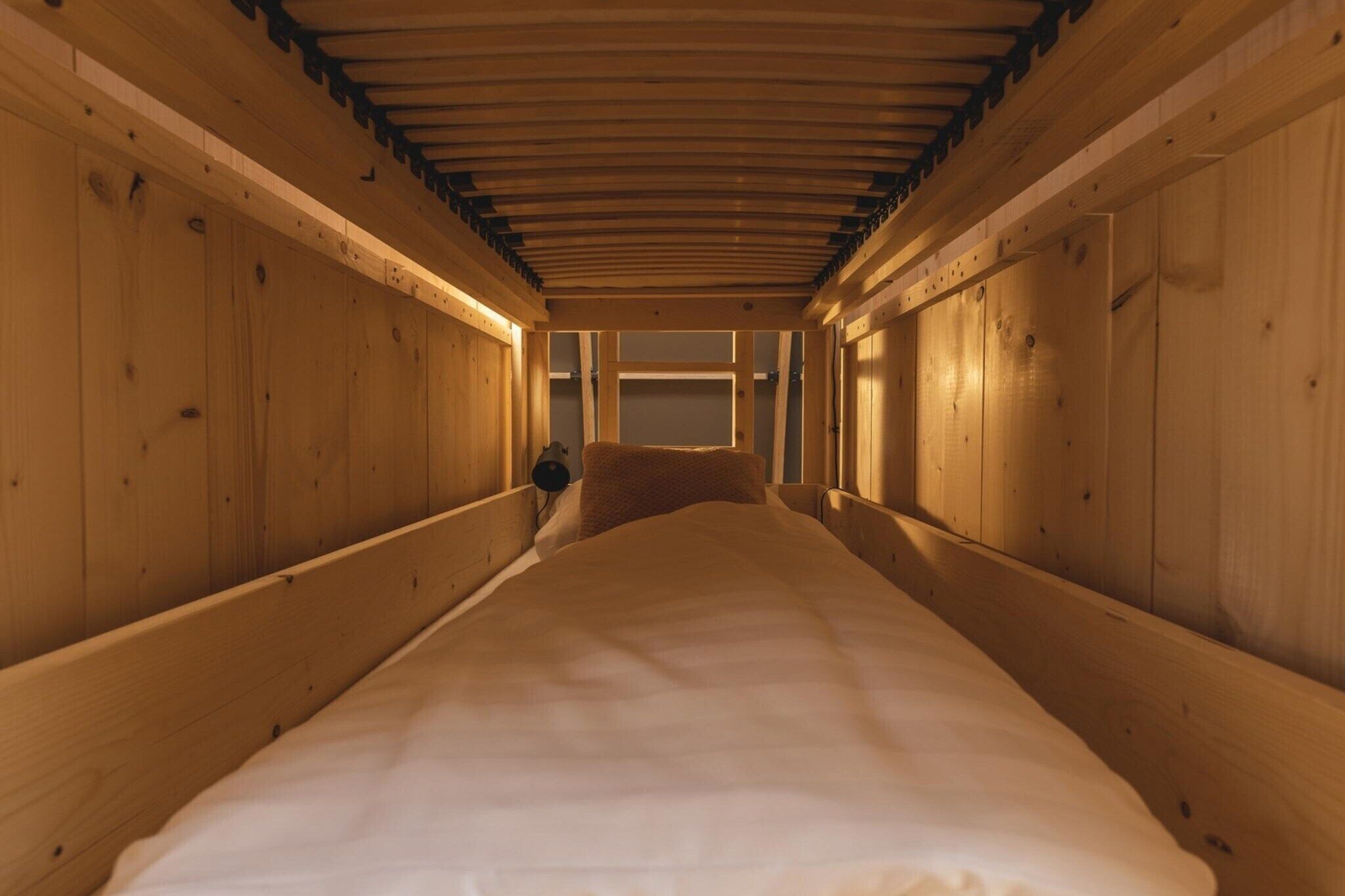 Een smal, houten interieur met een bed aan het einde, houten wanden en een schuine hemel.
