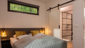 A bedroom with a bed, a window, a nightstand, and a shower area. - Home near National Park (Zuna)