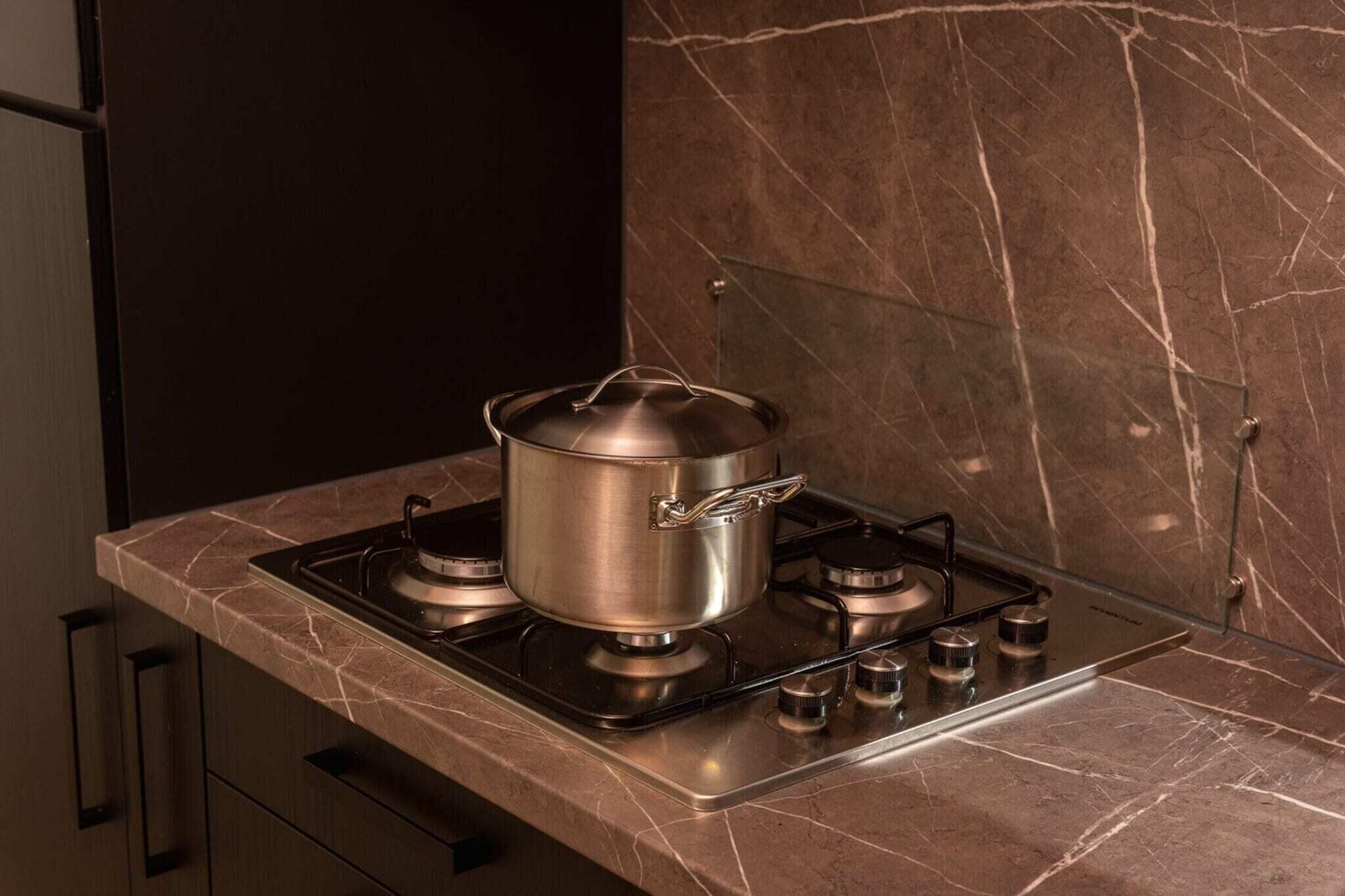 A kitchen with a gas stove, a pot on the burner, and a marble countertop.