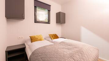A bedroom with a bed, two nightstands, a window with blinds, and built-in cabinets.