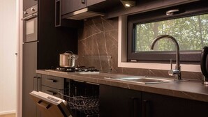 A modern kitchen with dark cabinetry, a built-in stove, a sink, and a window above the sink. - Home near National Park (Zuna)