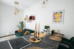 Una sala de estar moderna con un sofá verde, una mesa de centro de vidrio, piso de mármol y una lámpara fijada a la pared.