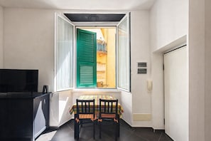 A small room with a table and chairs, a TV, and a window with green shutters.