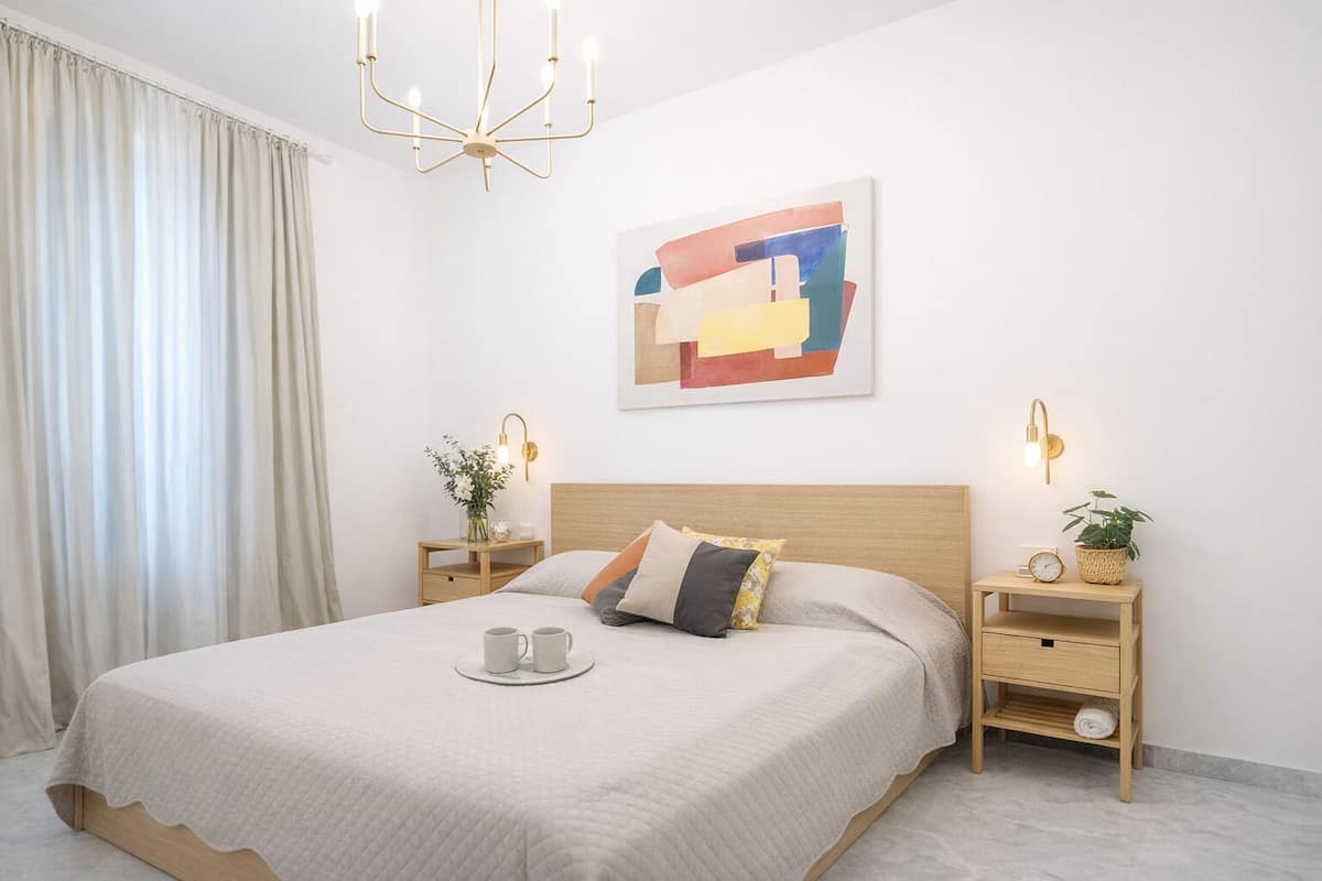 Ein ordentlich eingerichtetes Schlafzimmer mit einem Bett, Nachttischen, einem Wandbild und einer Chandelier.