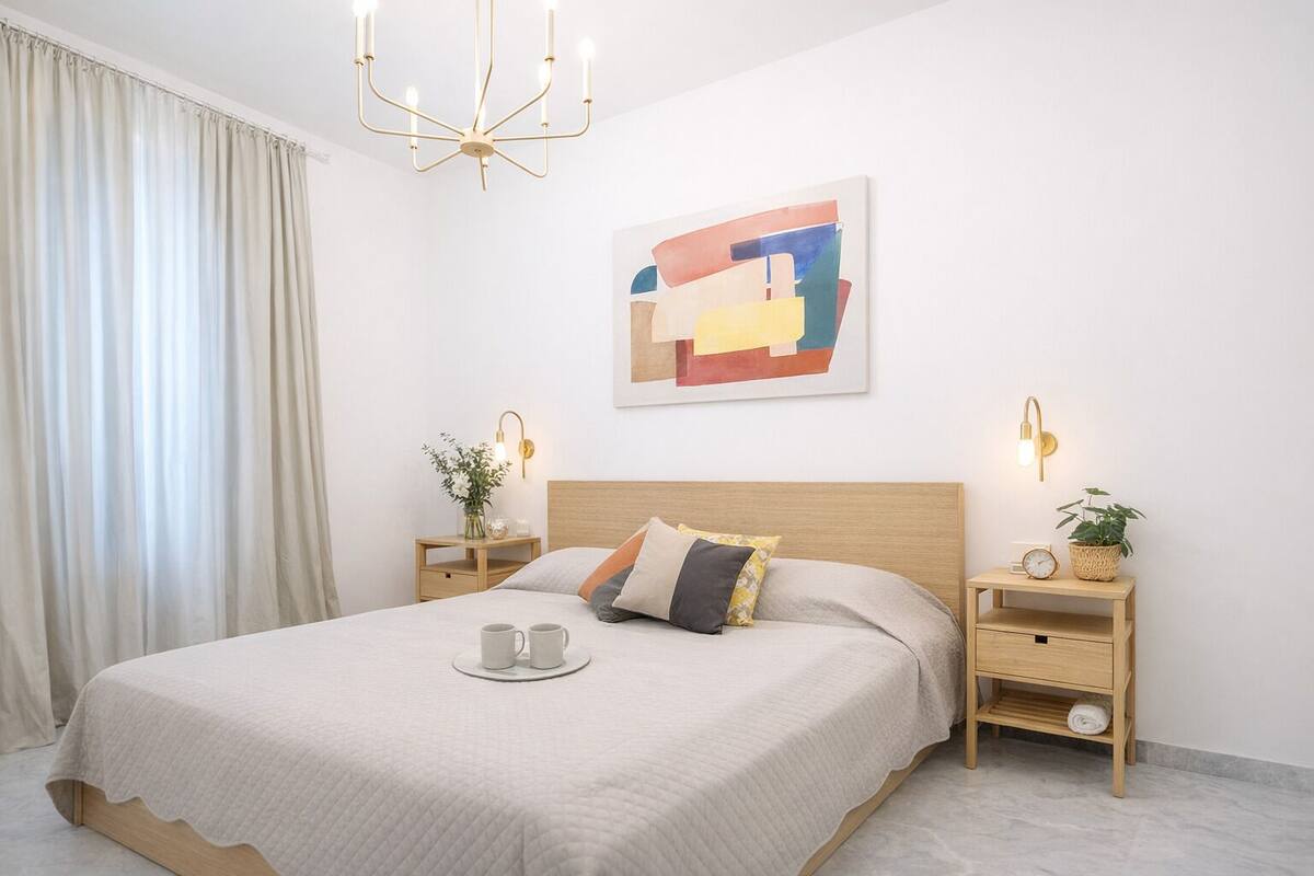 A neatly arranged bedroom with a bed, bedside tables, a wall-mounted artwork, and a chandelier.