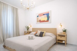 A neatly arranged bedroom with a bed, bedside tables, a wall-mounted artwork, and a chandelier.