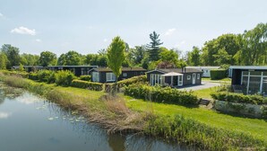 Een rij moderne, gelijkvloerse blokhutten met grote ramen, gelegen aan een rustig waterlichaam, omgeven door weelderige begroeiing.