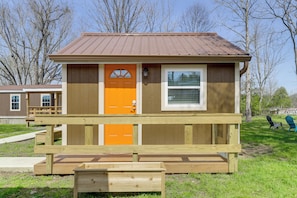 Ein kleines Holzgebäude mit einem braunen Dach, einer einzelnen orangefarbenen Tür und einem Fenster.