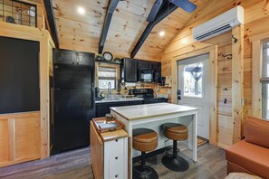 Kompakti keittiö, jossa on puiset kaapit, musta jääkaappi, mikroaaltouuni ja pieni keittiösaareke, jonka ympärillä on jakkaroita.