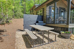 Une cabane en bois dotée d’un patio comprenant un barbecue, une table de pique-nique et des bancs.