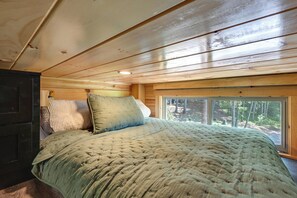 Une chambre à coucher avec un lit, des oreillers, une fenêtre et une vue sur l’extérieur.