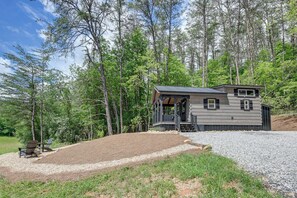 Une cabane dotée d’un porche, entourée d’arbres, et une allée menant à la maison, recouverte de gravier.