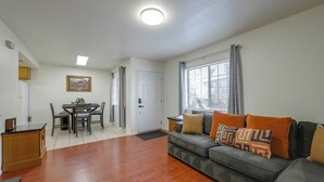 A living room with a sofa, a dining table with chairs, a kitchen area, and a window with curtains. - Shop, Dine, Hike, Explore Dtwn! Flagstaff Getaway (Flagstaff)