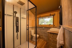 Une salle de bain avec une douche à parois de verre, des toilettes et un lavabo, avec une fenêtre au-dessus.