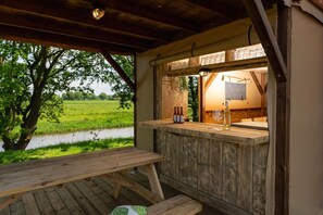 Ein Sitzbereich im Freien aus Holz mit Blick auf ein grünes Feld und einen Fluss.