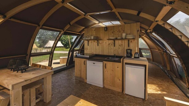 Un intérieur en bois comprenant une cuisine, une table à manger et une vue à travers le toit incurvé.