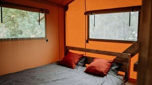 Un lit simple avec une tête de lit en bois, deux fenêtres et des murs orange.