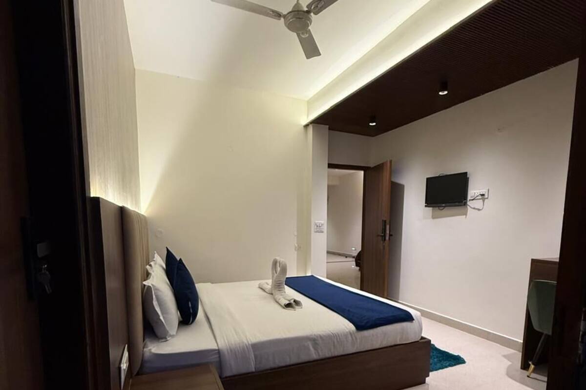 Un dormitorio moderno con una cama, un ventilador de techo, un televisor y una puerta que da a otra habitación.