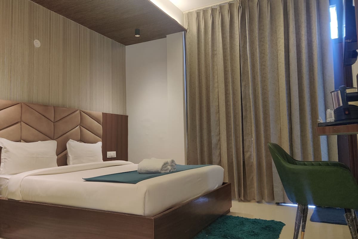 A hotel room with a bed, a desk with a chair, a ceiling fan, and curtains.