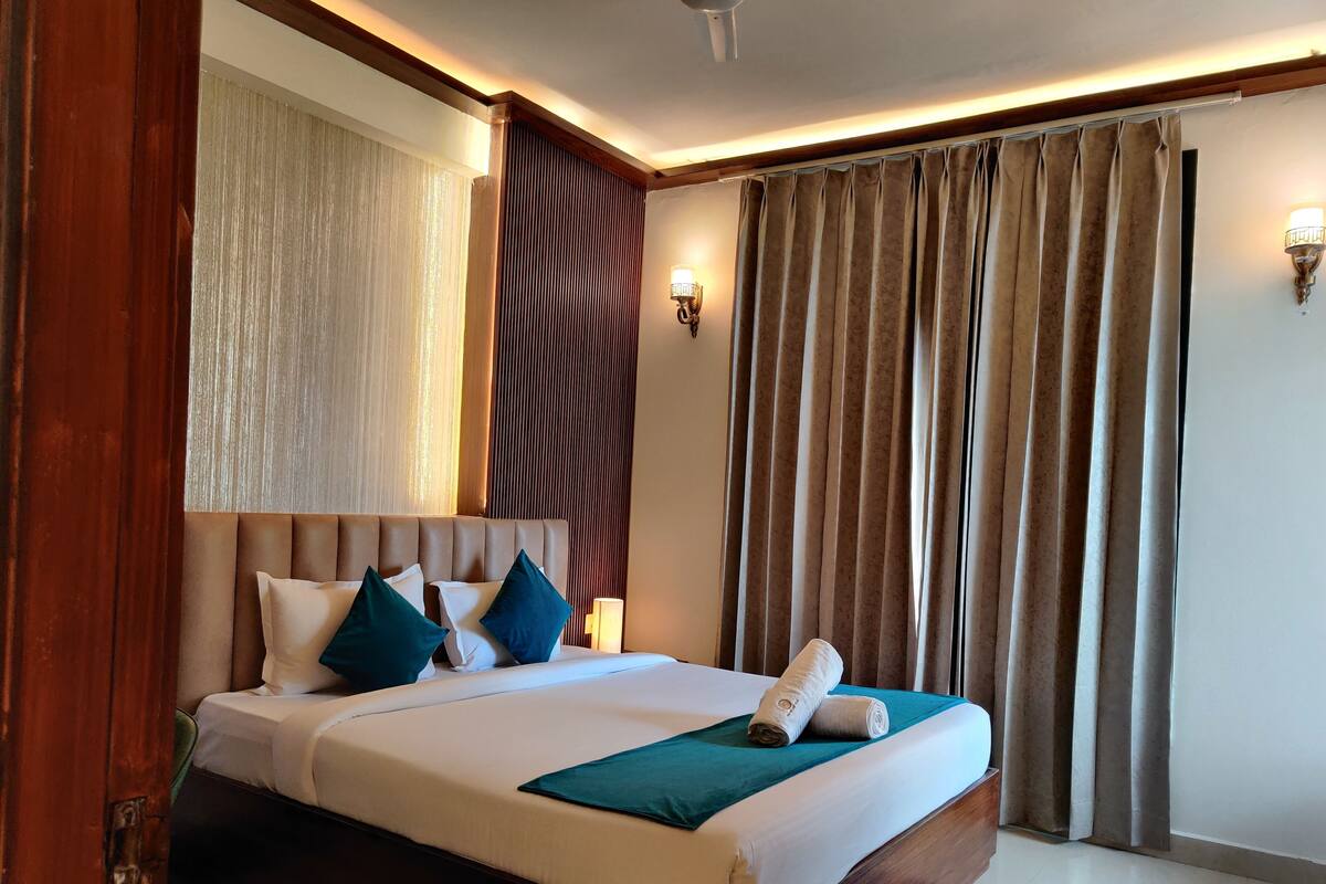 Habitación de hotel con una cama grande, cabecera de madera, luz de pared y ventana con cortinas.