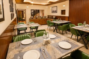 Un restaurante con varias mesas, sillas tapizadas de verde y una zona de bar al fondo.