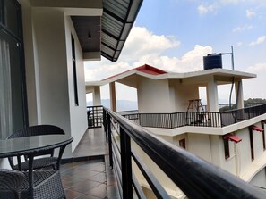 A balcony with a view of mountains, a tiled floor, and a table with chairs. - Hotel Heaven & Hills Kasauli (Kasauli)