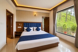 A modern bedroom with a large bed, wooden headboard, bedside tables, and a view of greenery through a window. - Hotel Heaven & Hills Kasauli (Kasauli)