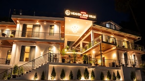 Un hotel de varios pisos con balcones, un letrero que dice 'Hotel Heaven and Hills', y una escalera que lleva a la entrada.
