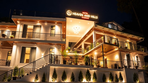 Un hotel de varios pisos con balcones, un letrero que dice 'Hotel Heaven and Hills', y una escalera que lleva a la entrada.