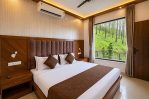 Habitación de hotel con una cama grande, cabecero de madera, mesitas de noche, equipo de aire acondicionado y ventana con vistas a un bosque.
