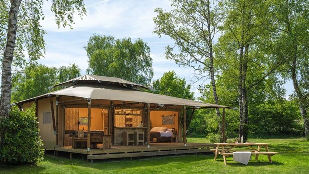 A wooden cabin with a porch, a dining table, and a picnic table. - Charming Safari Tent for Family Glamping (Zuna)