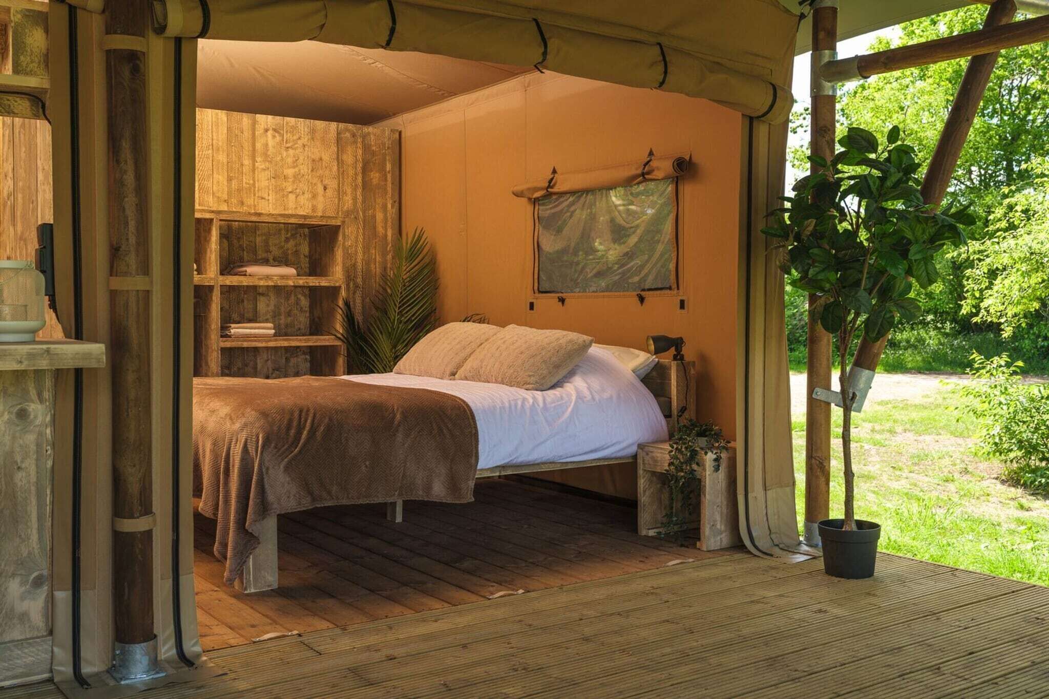 A rustic wooden tent with a bed, a shelf with books, and a window overlooking greenery.