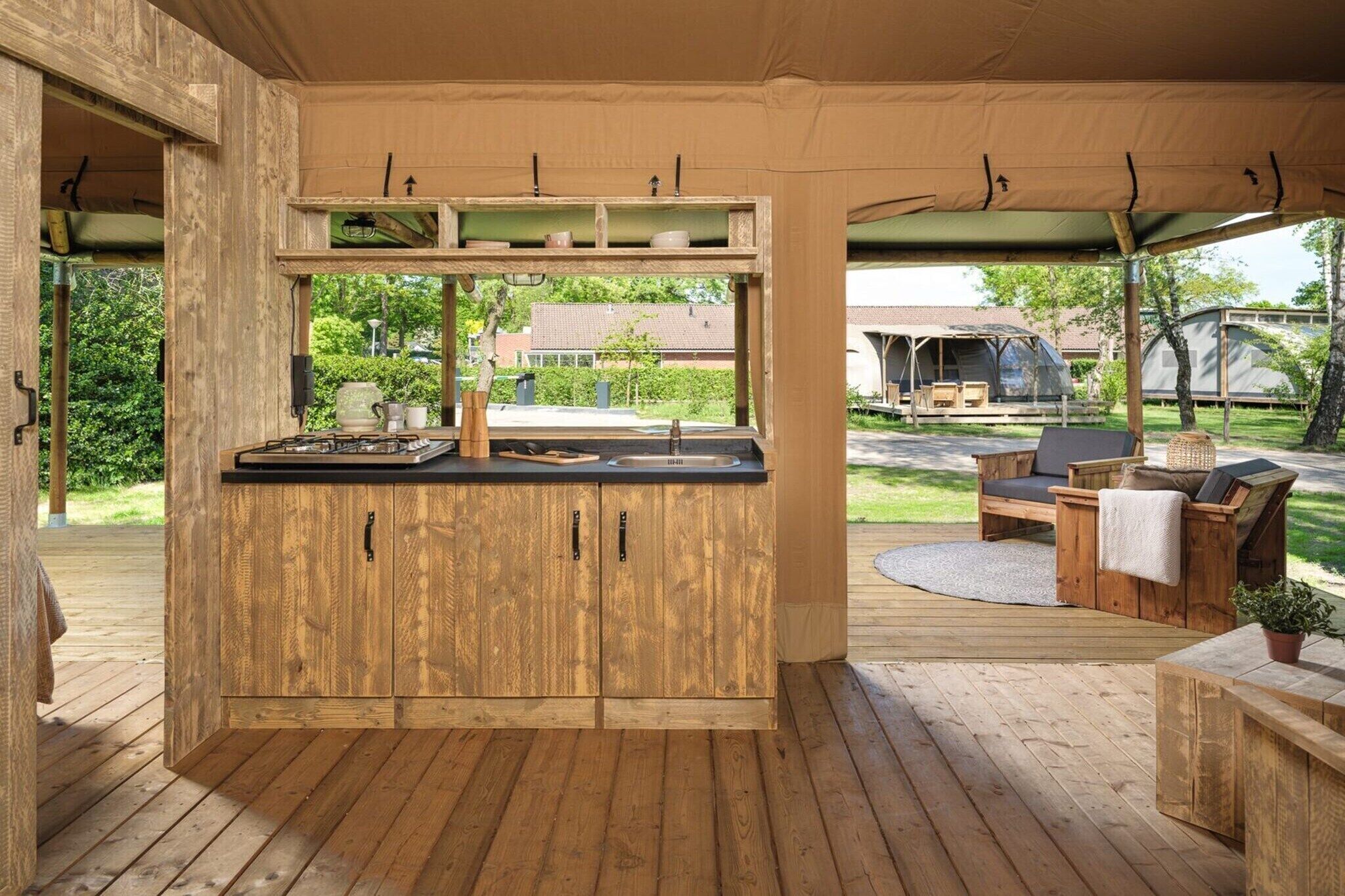 Een houten terras met een keukenhoek, zitplaatsen buiten en uitzicht op een woonwijk.