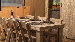 A wooden dining table set with plates, glasses, and a bottle of wine. - Charming Safari Tent for Family Glamping (Zuna)