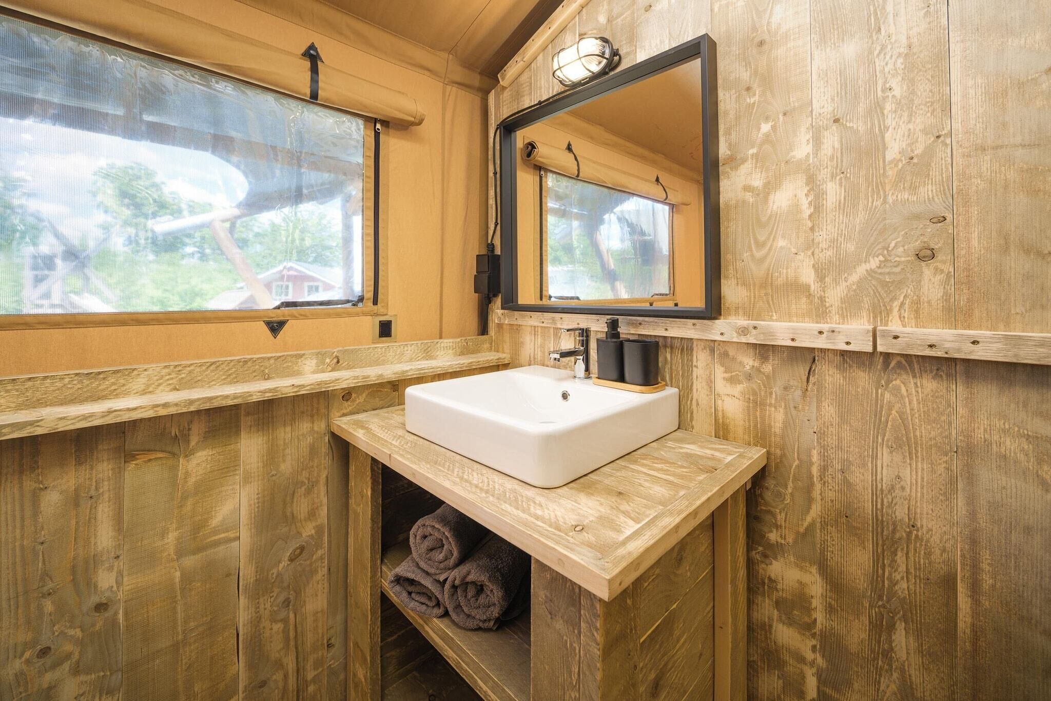 Ein Badezimmer einer Holzhütte mit einem weißen Waschbecken, einem Spiegel und einem Fenster.