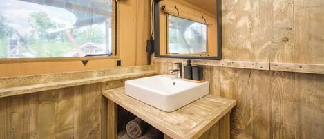 Baño de cabaña de madera con lavamanos blanco, espejo y ventana.