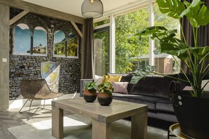 A cozy room with a stone wall, a wooden table, a black sofa, and a large potted plant. - Bungalow with Nursery and Playground (Zuna)