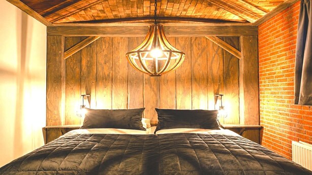 Ett rum med träpanel på väggarna, en säng, en hängande lampa och en vägg av tegelsten.