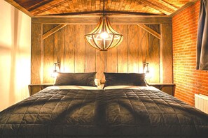 A wooden-paneled room with a bed, a hanging light fixture, and a brick wall.
