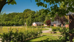 A rural setting with a pathway leading to a building with a sloped roof, surrounded by greenery and trees. - Six-Person Wellness Farmhouse (Zuna)