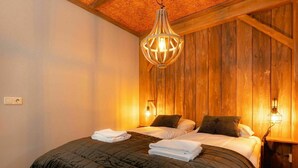 A room with a wooden wall, a bed with two pillows, a hanging light fixture, and a bedside table with a lamp. - Six-Person Wellness Farmhouse (Zuna)