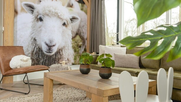 A cozy living room with a large sheep mural, a sofa, a coffee table, and a chair. - Six-Person Wellness Farmhouse (Zuna)