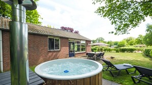 A hot tub in a backyard with a brick house, outdoor furniture, and a wooden deck.
