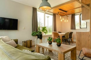Ein modernes Wohnzimmer mit einer Couch, einem Esstisch und Stühlen. Ein Fernseher ist an der Wand befestigt und auf dem Tisch stehen Zimmerpflanzen.