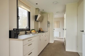 A narrow kitchen with a window, a coffee maker, a fruit bowl, and a stove. - Luxury Family Lodge with Hot Tub (Zuna)