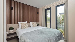 A modern bedroom with a large bed, a wooden slat wall, a small plant, and a view through the window. - Luxury Family Lodge with Hot Tub (Zuna)