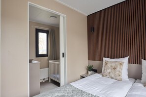 A bedroom with a bed, a bedside table, a nightstand, a window, a door, and a wooden panel wall. - Luxury Family Lodge with Hot Tub (Zuna)