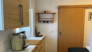 Eine kleine Küche mit Kaffeemaschine, Holzschränken, einem Waschbecken und einem kleinen Regal mit Tassen.